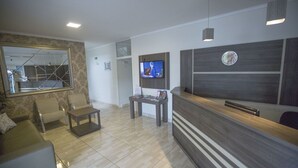 Ein Empfangsbereich mit einem Holztresen, einem an der Wand montierten Fernseher und einer Sitzecke mit zwei Sesseln.