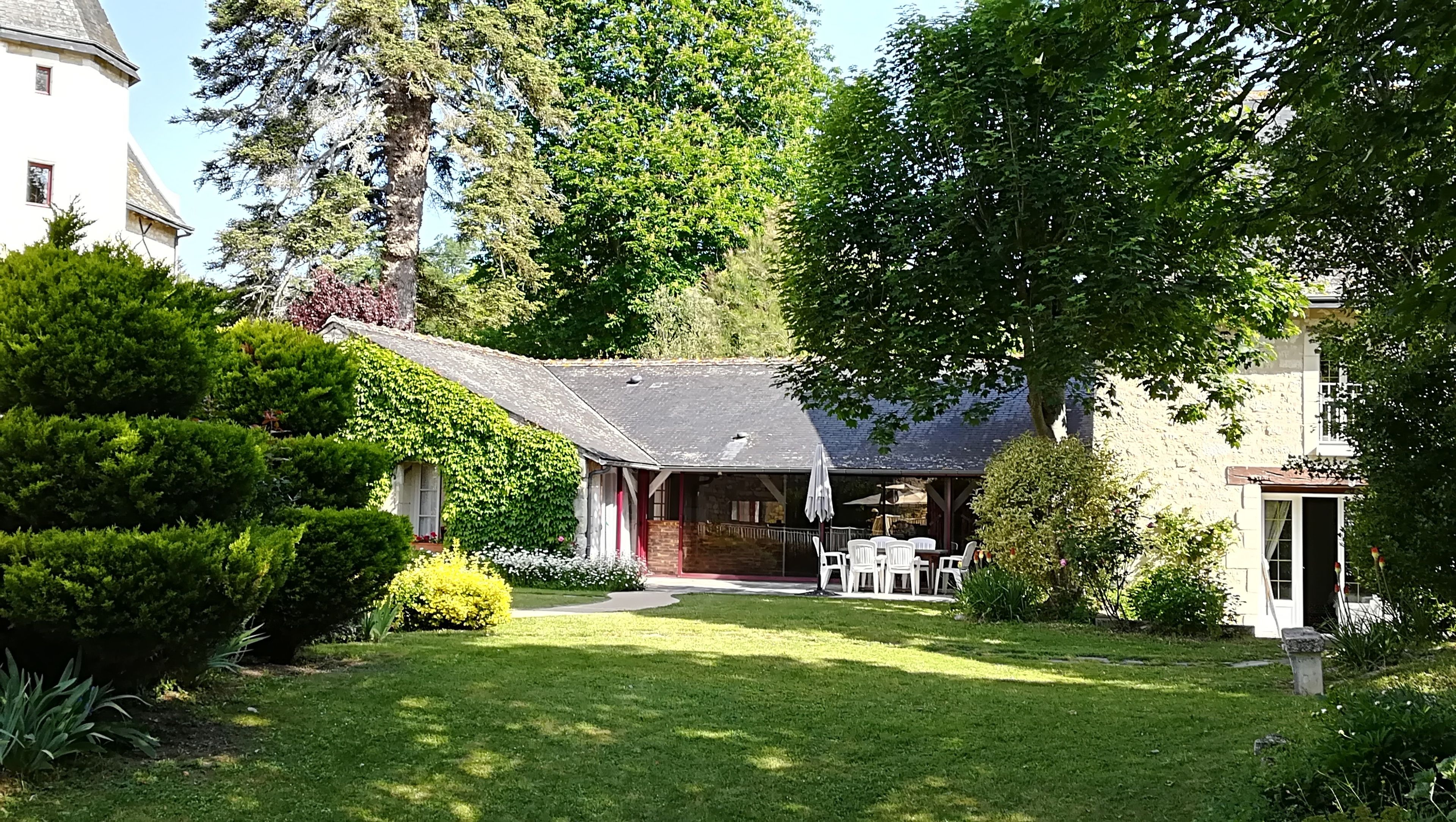 A traditional stone building with a sloped roof, surrounded by lush greenery and a well-maintained lawn.