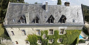 A large, historic building with a steeply pitched roof, multiple dormer windows, and a swimming pool in the foreground. - Manoir de L'abbaye (Seuilly)