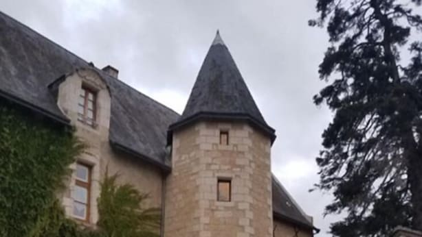 Een stenen toren, verbonden met een gebouw met klimopbedekte muren en een verzorgd gazon.