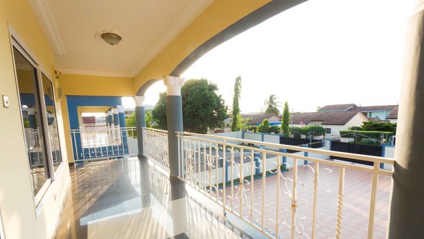 A balcony with a metal railing, a tiled floor, and a view of the surrounding neighborhood. - Jacksonfields Apartments (Accra)
