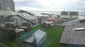 A rooftop terrace with a view of the sea, featuring a glass table, wicker furniture, and a green lawn. - The Castle Apartments (Castletown)