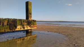 A beach with a weathered wooden structure, calm water, and a clear sky. - The Castle Apartments (Castletown)