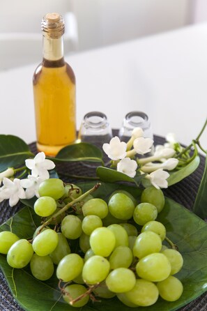 A bottle of olive oil, a plate of green grapes, and white flowers on a woven mat. - Elychryson (Hersonissos)