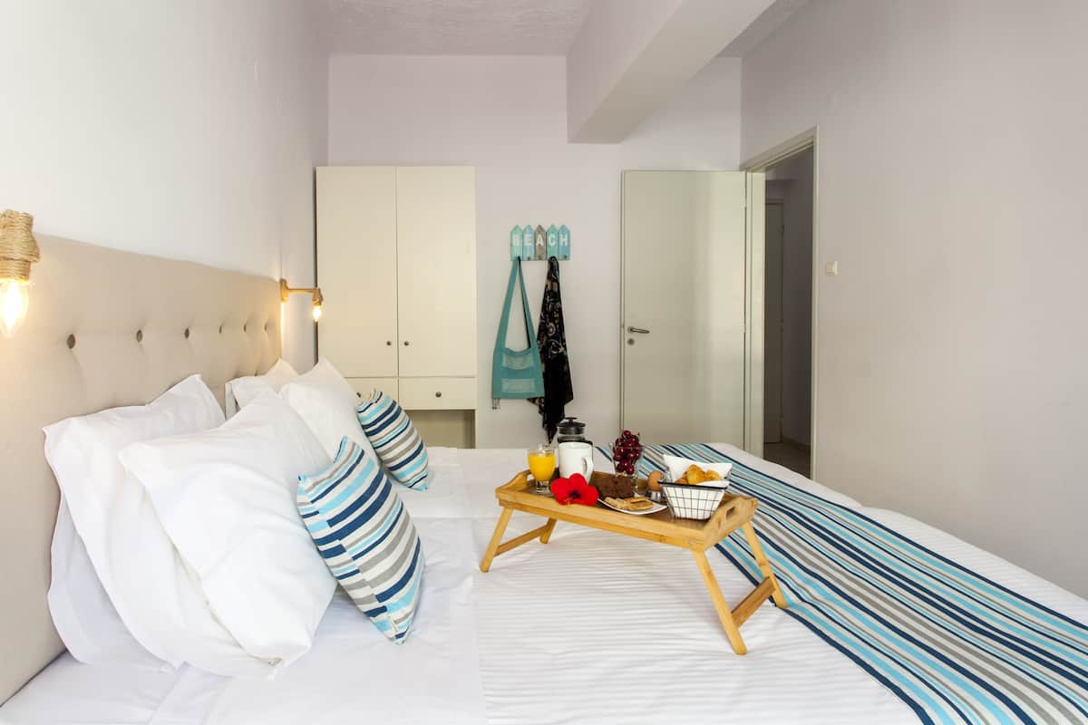 A neatly made bed with striped pillows, a bedside table with a tray of breakfast items, and a wardrobe with a towel hanging.