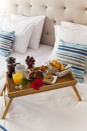 A breakfast tray with coffee, juice, bread, and pastries on a bed with striped pillows. - Elychryson (Hersonissos)