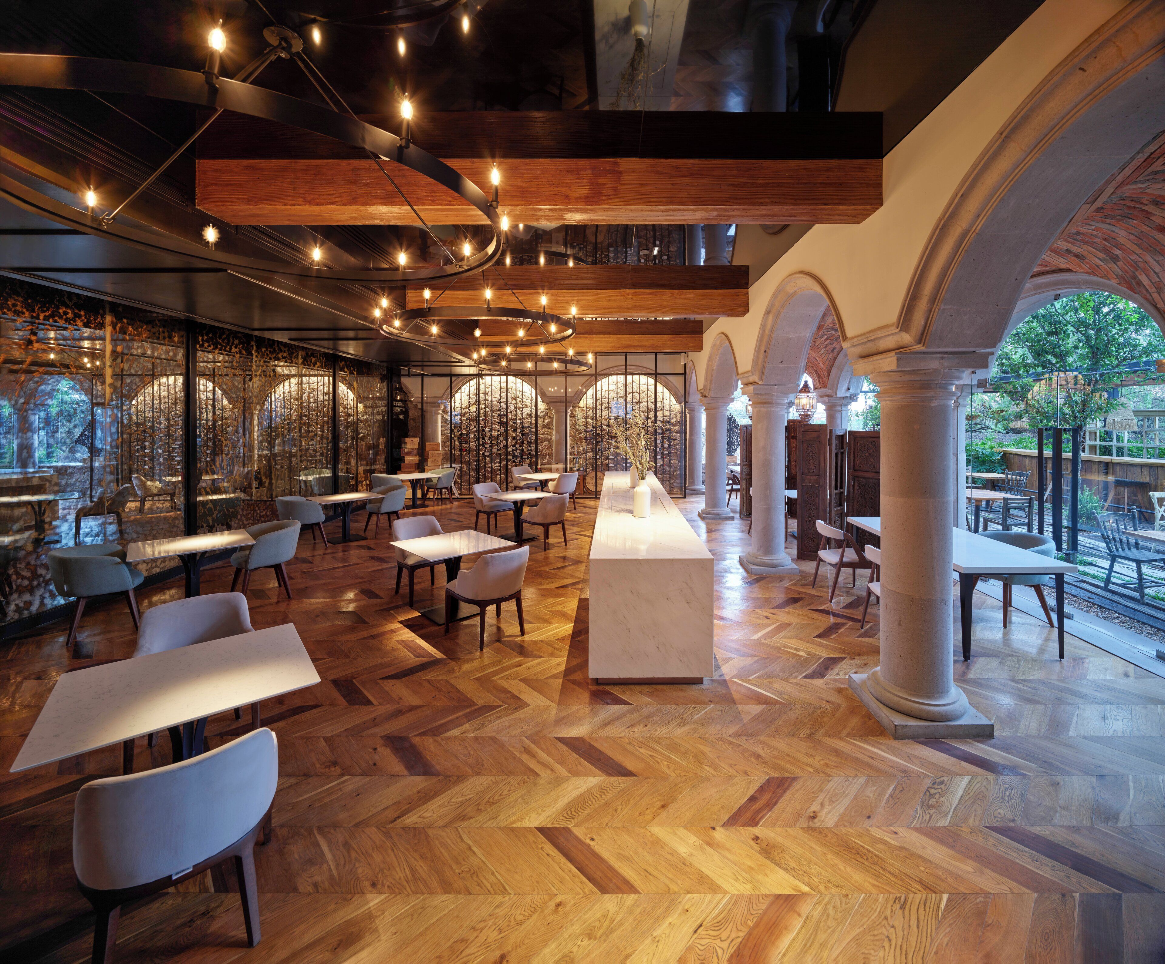A spacious restaurant with wooden flooring, multiple tables and chairs, and a view of the outdoors through large windows.