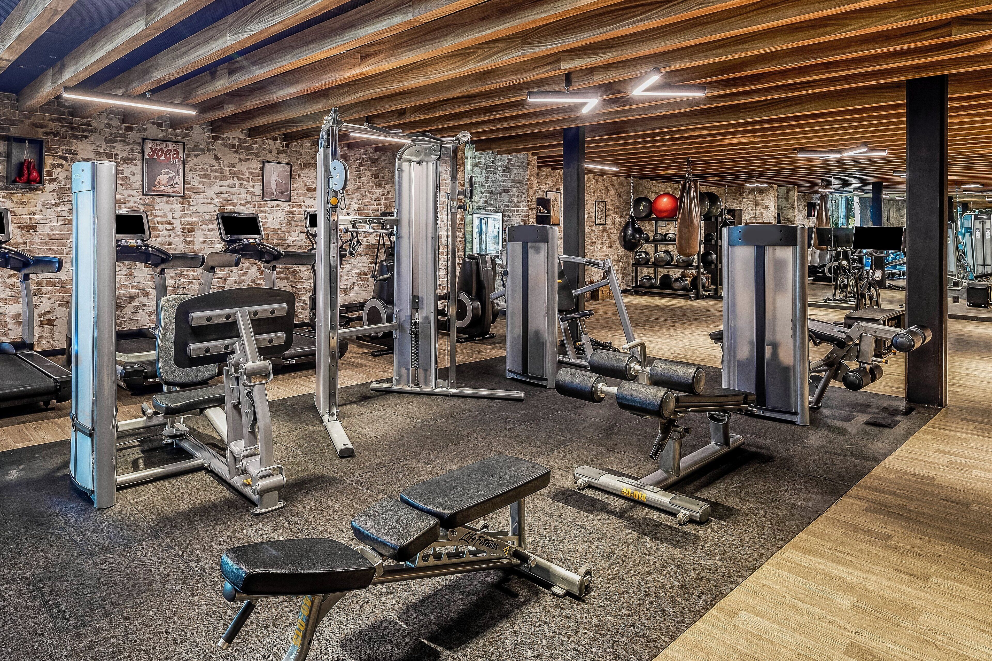 Un gimnasio con equipo de ejercicio diverso, piso de madera y paredes de ladrillo.