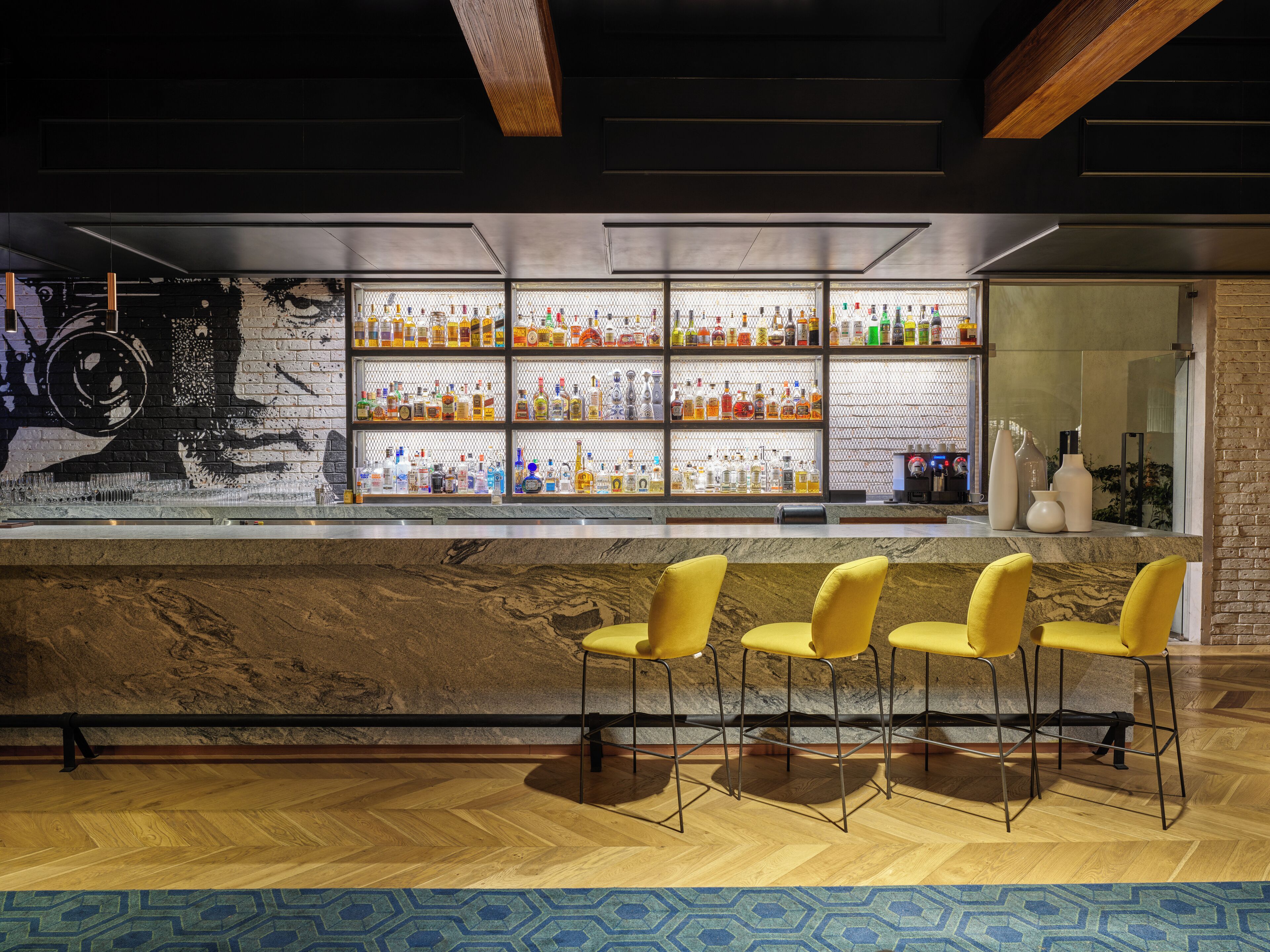 A bar area with a marble countertop, yellow bar stools, and shelves stocked with bottles.