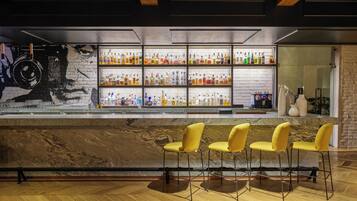A bar area with a marble countertop, yellow bar stools, and shelves stocked with bottles.