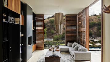 Una sala de estar moderna con un amplio sofá modular, una mesa de centro y una estantería. La habitación tiene un ventanal con vistas a una colina.