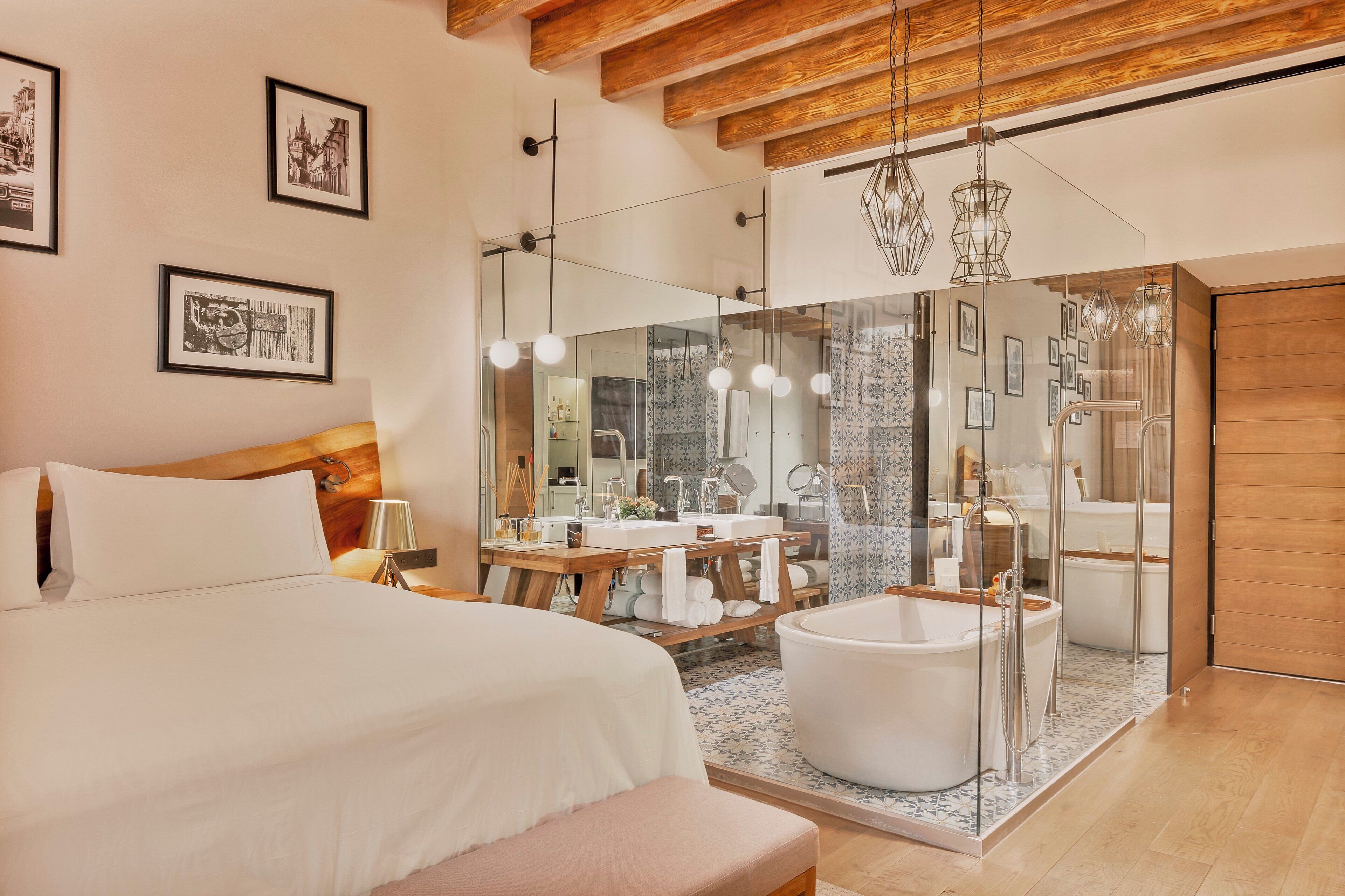 Quarto de hotel moderno com uma cama grande, chuveiro em cabine de vidro, banheira e teto de madeira.