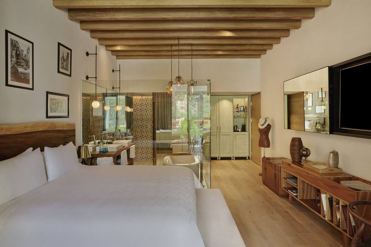 Quarto com uma cama grande, teto de madeira, banheiro com chuveiro, área de jantar e televisão na parede.