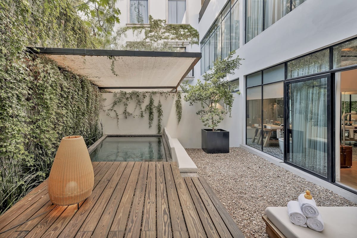 Uma área externa moderna com um deck de madeira, uma piscina pequena e um espaço de estar com toalhas.