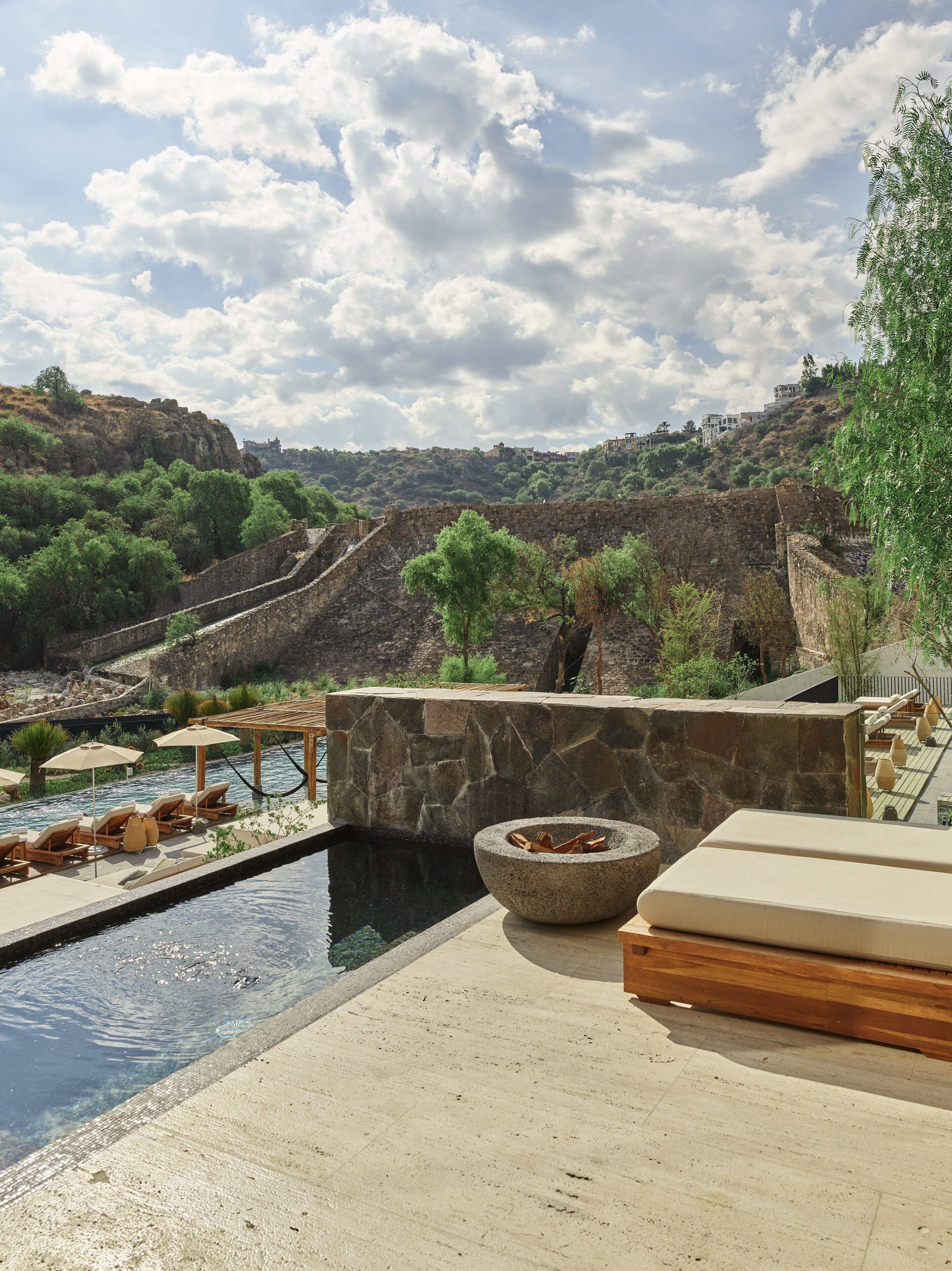 Un área de piscina con paredes de piedra, sillones de descanso y una chimenea.