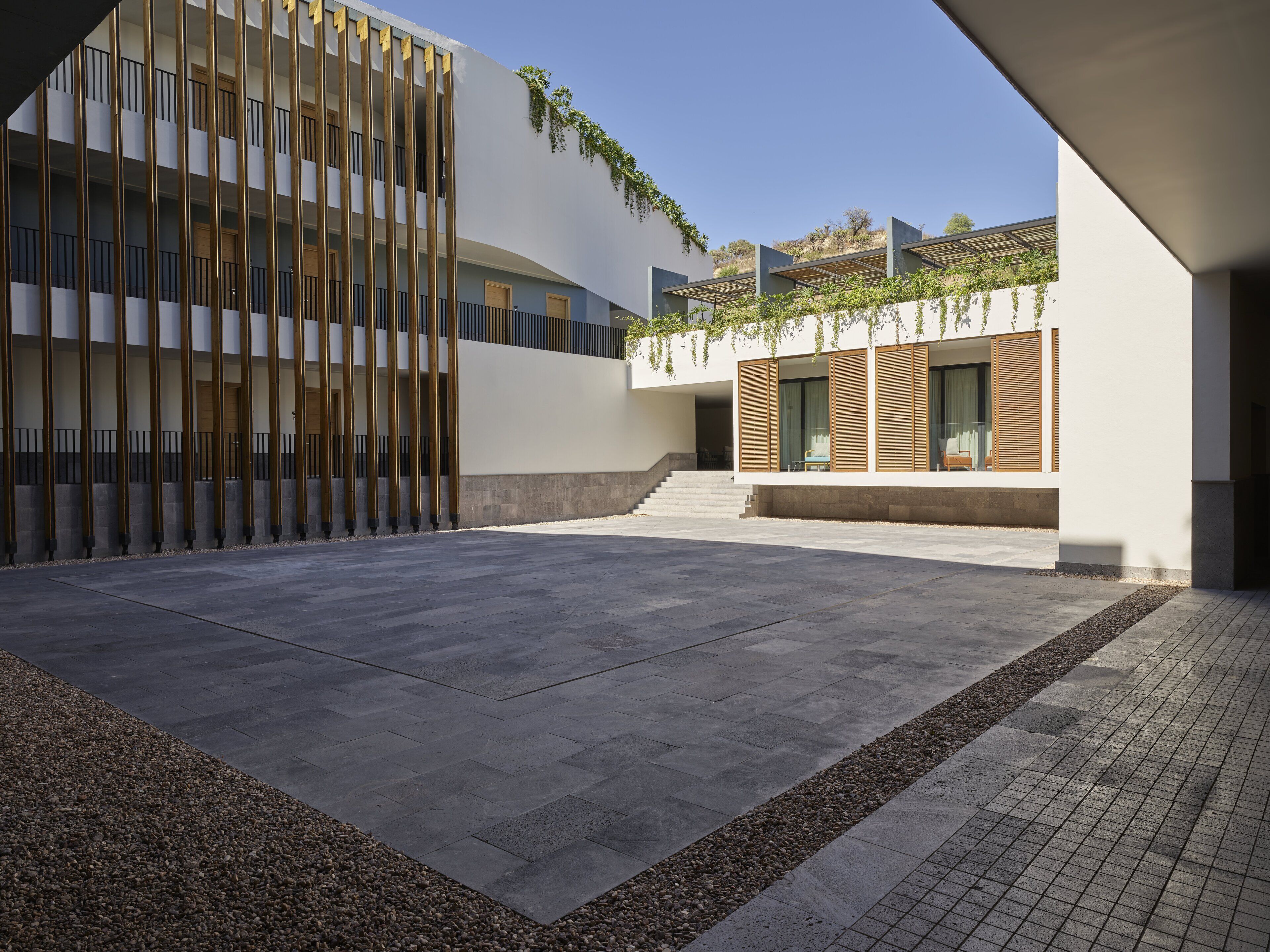 A modern building with a courtyard, featuring a curved facade, wooden slats, and a small seating area with a table and chairs.