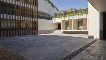 A modern building with a courtyard, featuring a curved facade, wooden slats, and a small seating area with a table and chairs.