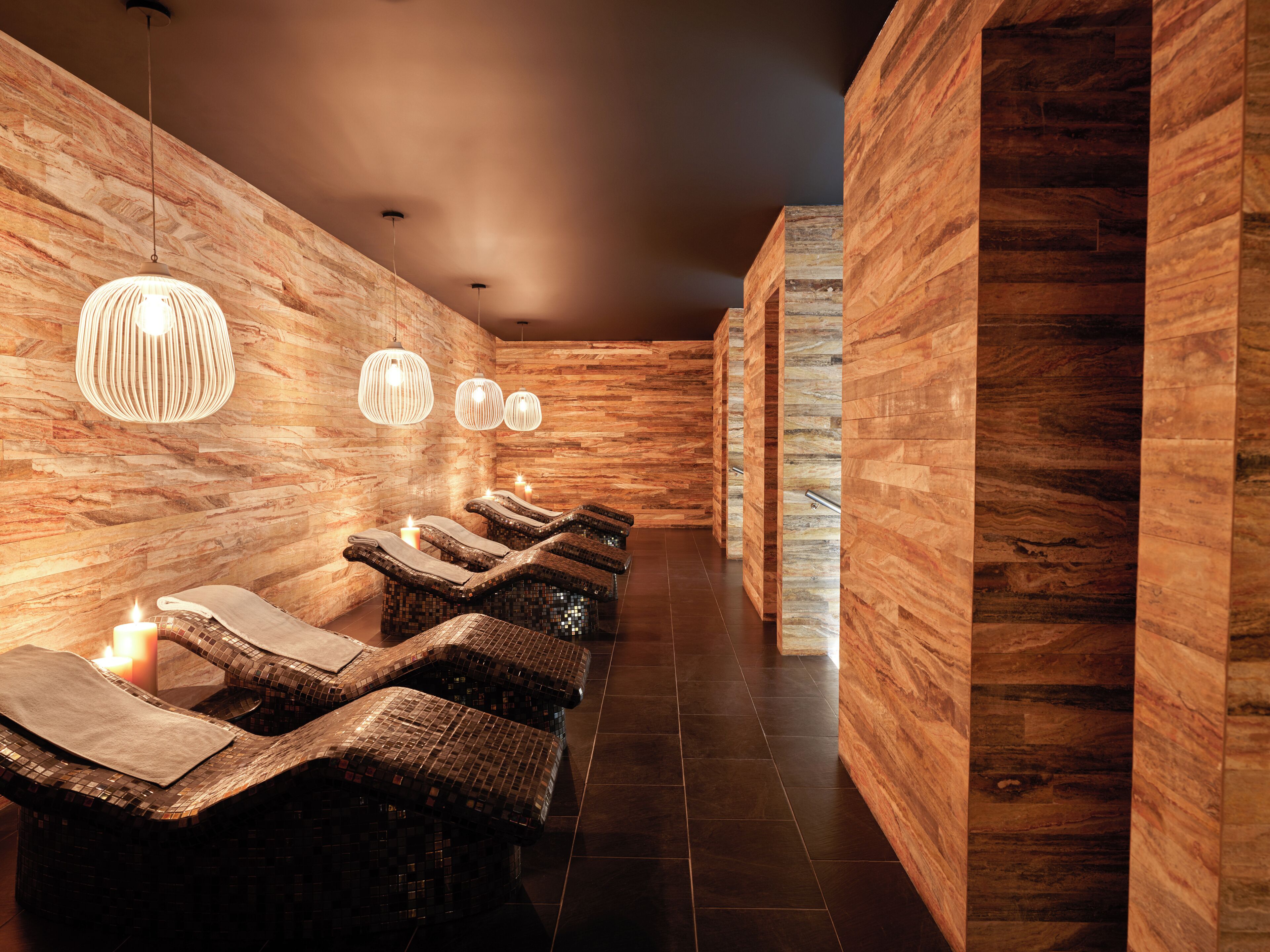 Un cuarto de spa con paredes de madera, una fila de camillas de masaje y lámparas colgantes.