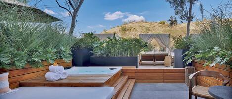 Una terraza de madera con un jacuzzi, un banco y una mesa.