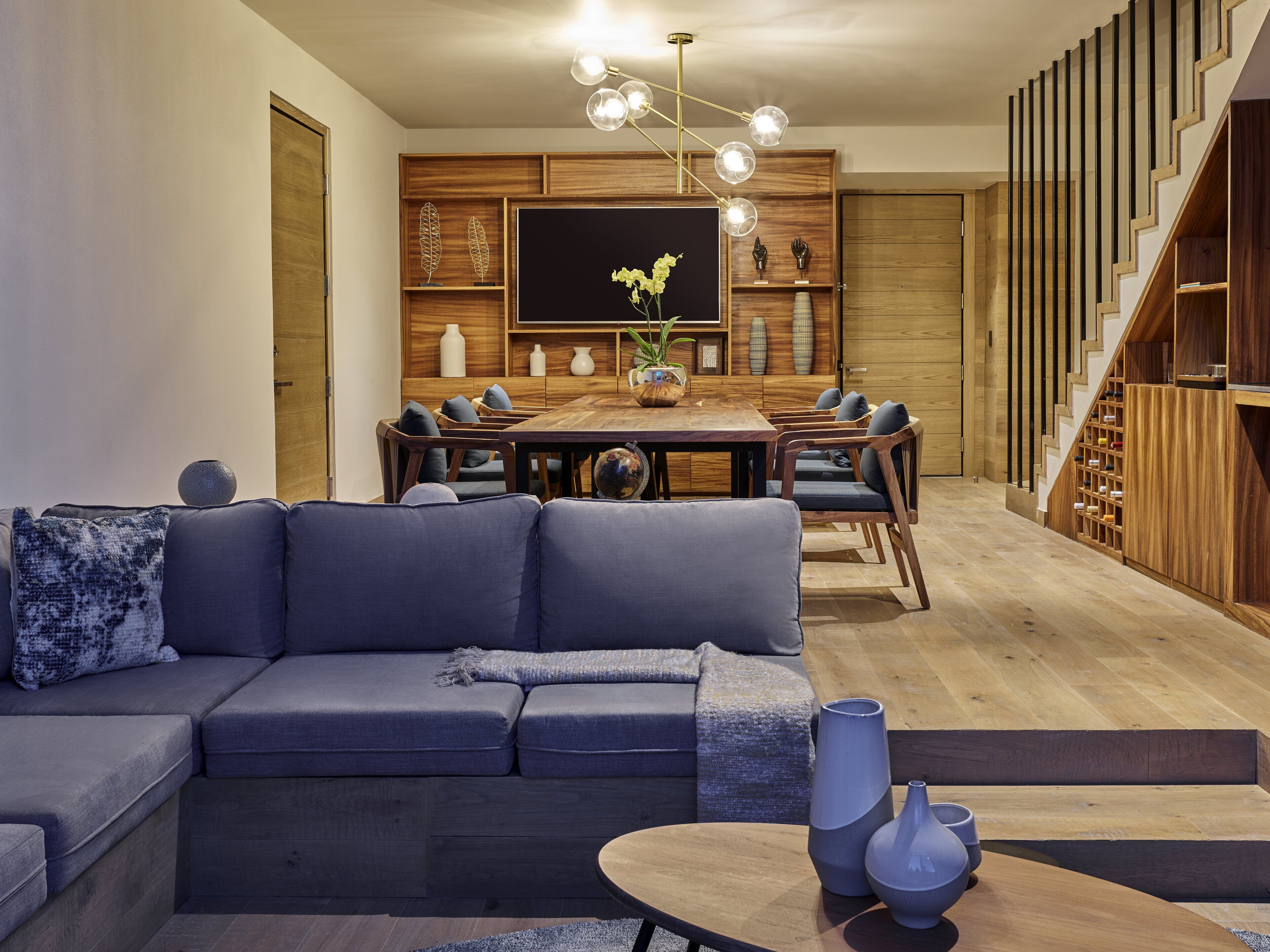 Una sala de estar moderna con un sofá modular, una mesa de comedor y una escalera con barandilla de madera.