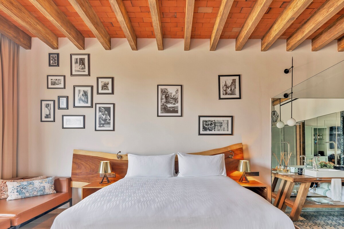 Ein Hotelzimmer mit einem großen Bett, einem Holzkopfteil, Nachttischen mit Lampen, einem Spiegel und gerahmten Bildern an der Wand.