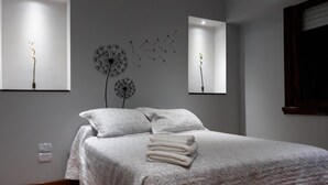 Una cama bien tendida con ropa blanca y una toalla doblada, una lámpara de pared y un adorno en la pared.