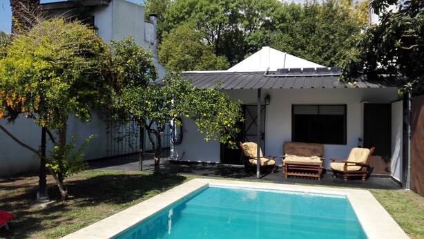 Una piscina con un área de patio, un espacio de descanso cubierto y un pequeño árbol con frutos.