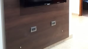 Un televisor montado en la pared con un diseño floral encima, dos tomas de corriente debajo y un marco de puerta de madera a la derecha.