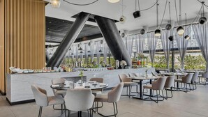 A modern restaurant interior with round tables, chairs, and a central counter with food and drink items.