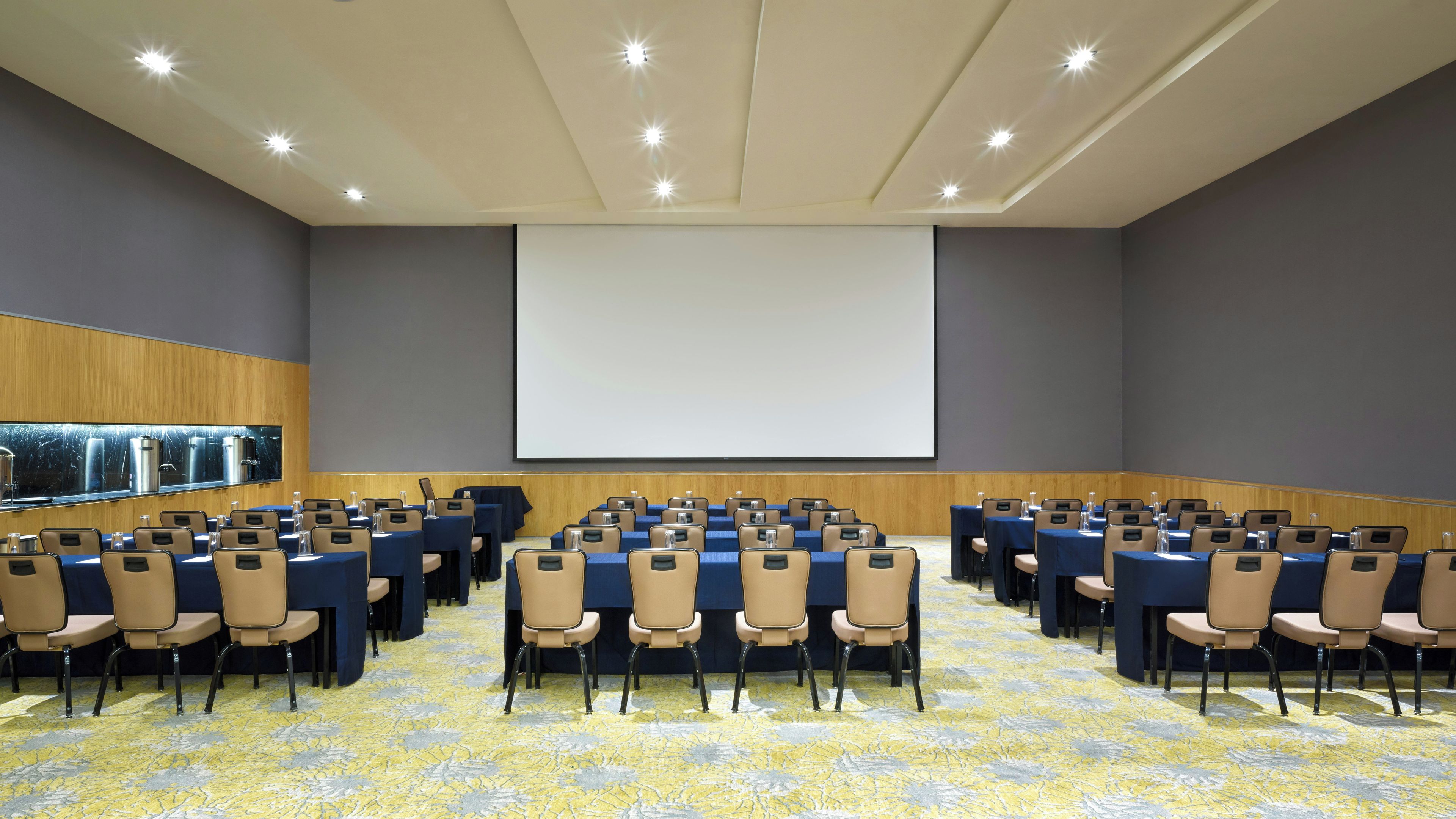 A conference room with rows of chairs, a large screen, and a water dispenser.