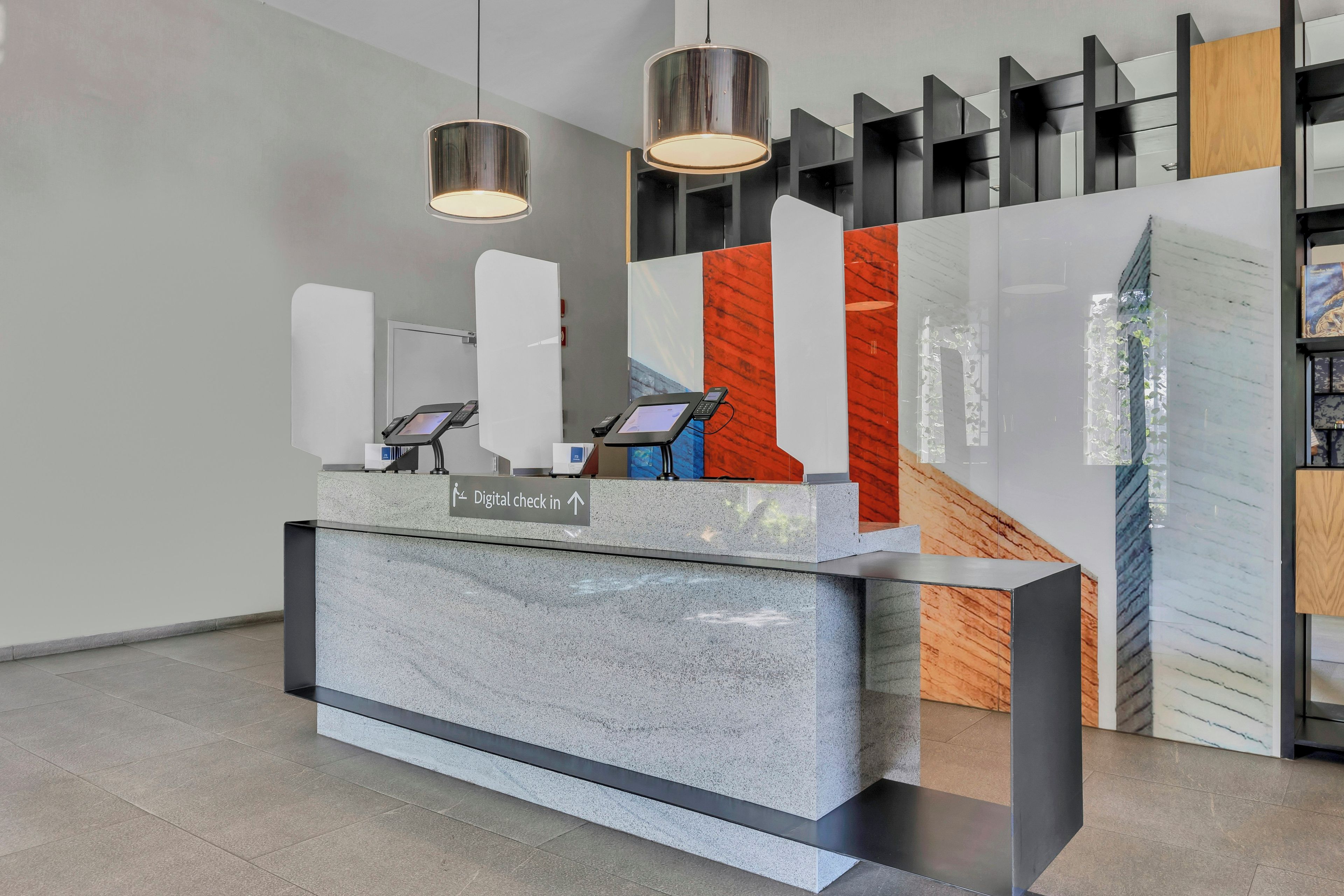 A reception desk with digital check-in kiosks, a sign indicating the direction for digital check-in, and a modern interior design with geometric shelving and pendant lighting.