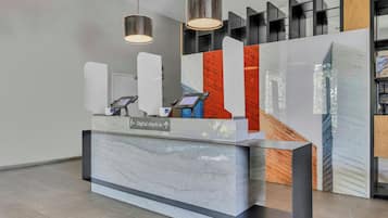 A reception desk with digital check-in kiosks, a sign indicating the direction for digital check-in, and a modern interior design with geometric shelving and pendant lighting.