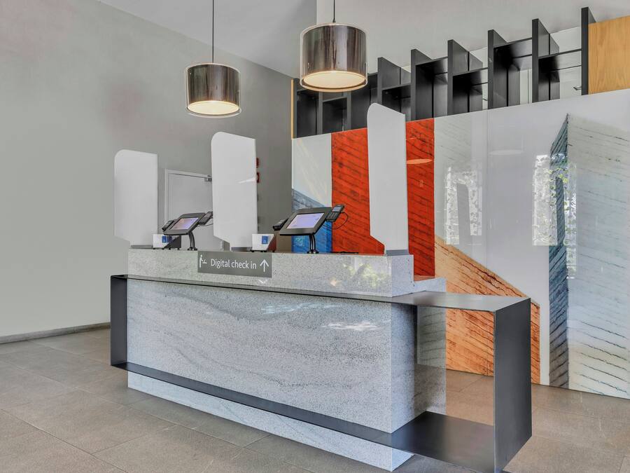 A reception desk with digital check-in kiosks, a sign indicating the direction for digital check-in, and a modern interior design with geometric shelving and pendant lighting.