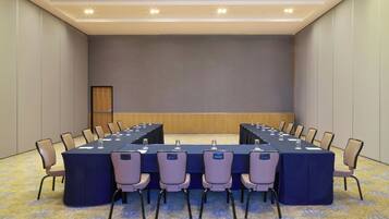 Un salón de conferencias con una larga mesa, sillas y una pantalla de proyector.