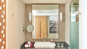 A modern bathroom with a wooden vanity, a large mirror, and a view of a railway track through the mirror. - Fiesta Americana México Satélite (Tlalnepantla de Baz)