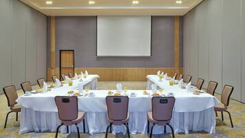 Un salón de conferencias con una mesa larga, sillas y una pantalla de proyector.