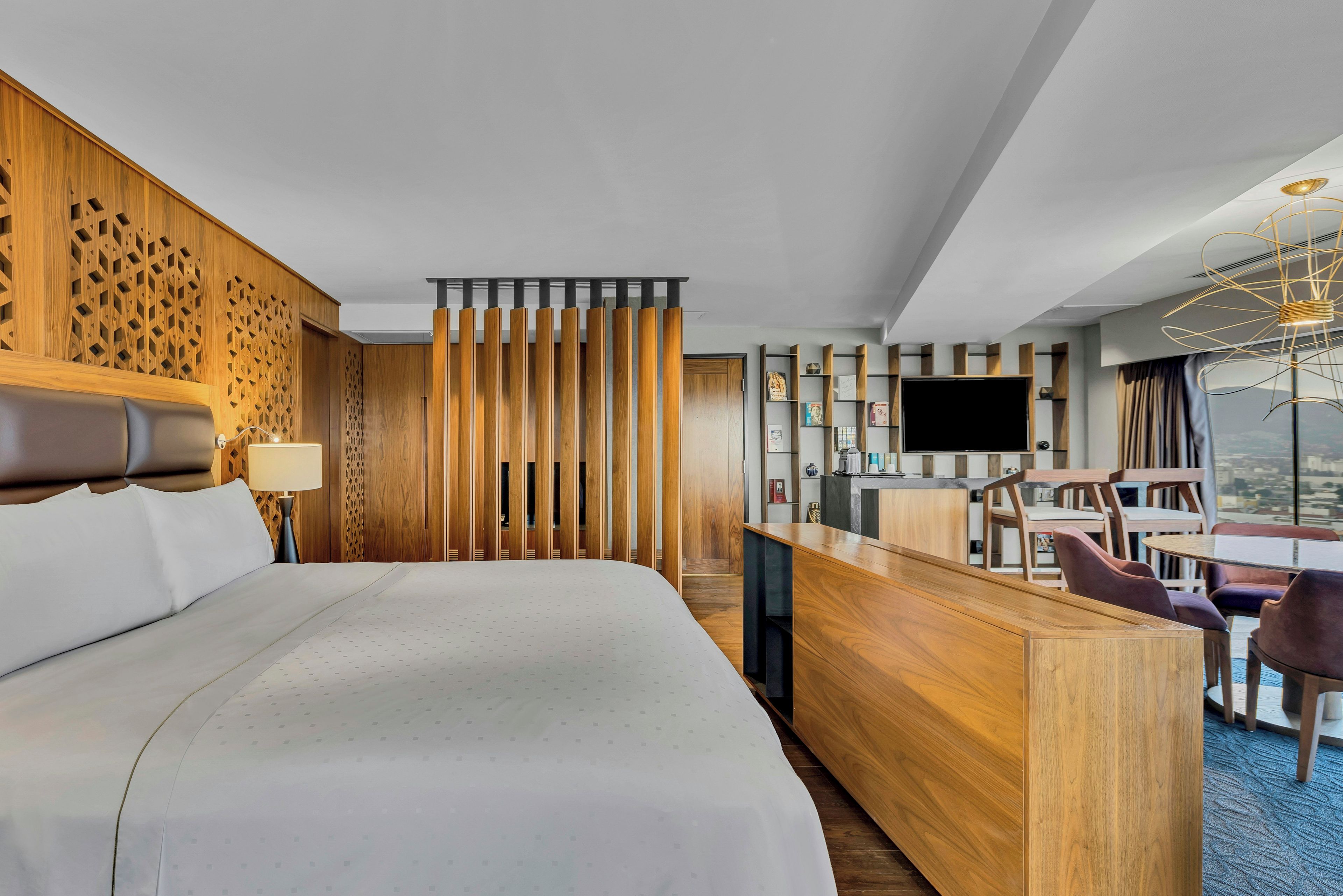 A hotel room with a large bed, a desk with chairs, a TV, and a city view.