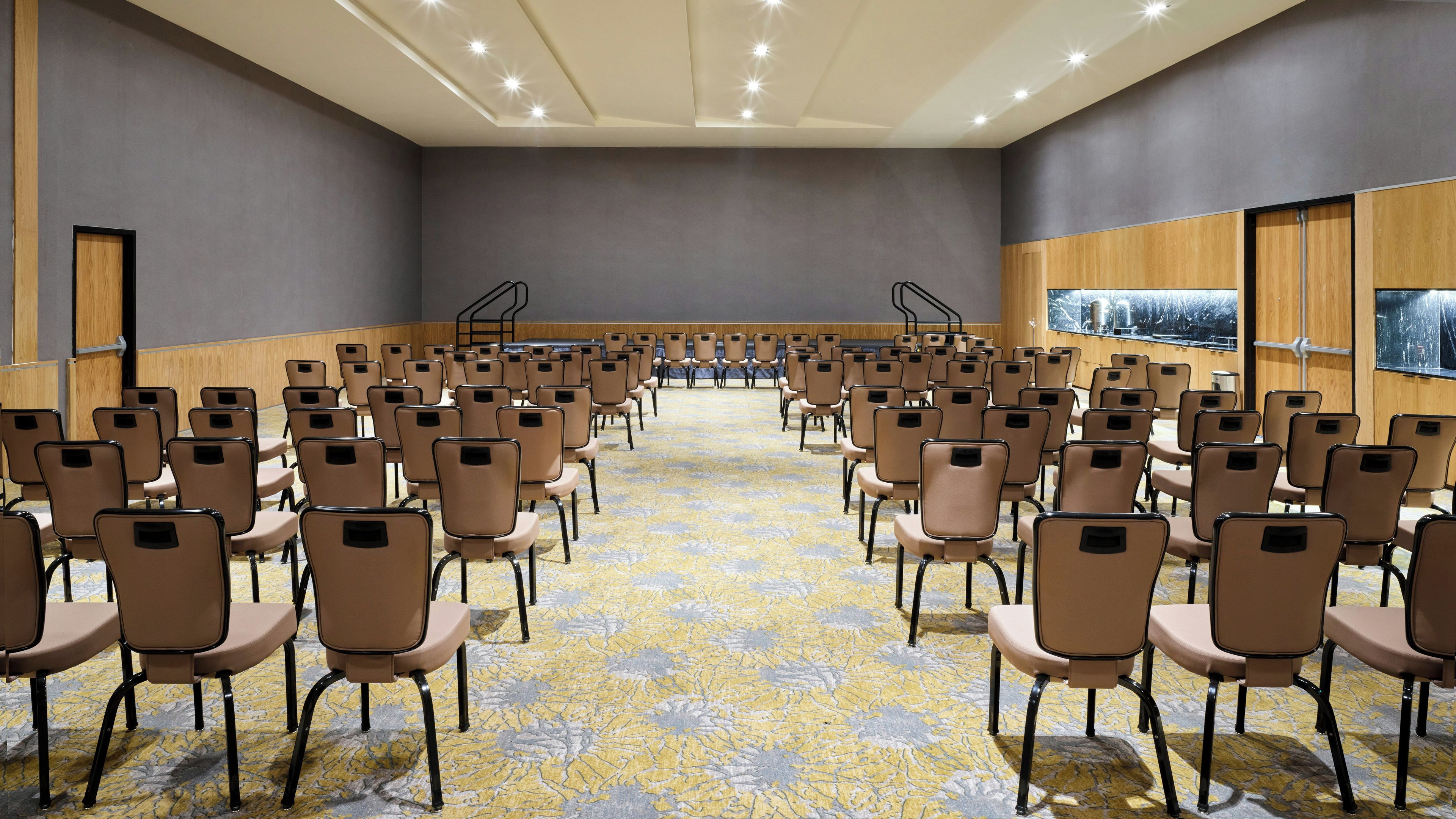 Un salón de conferencias con filas de sillas, piso alfombrado y paneles de madera.