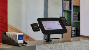 A payment terminal with a screen displaying a welcome message, a mobile phone, and a card reader with a cardholder's name on it.