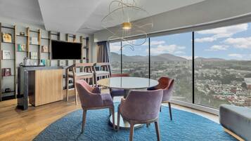 A modern living room with a round table, purple chairs, a large window with a city view, a flat-screen TV, and a unique ceiling light fixture.