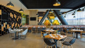A modern restaurant interior with high ceilings, geometric wall panels, and a mix of seating arrangements including tables and booths.