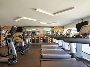 Uma academia com vários equipamentos de ginástica cardiovascular, incluindo esteiras e bicicletas ergométricas, dispostos em fileiras.