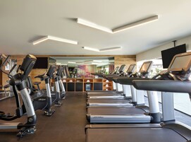 Un gimnasio con varias máquinas de cardio, incluyendo cintas de correr y bicicletas estáticas, dispuestas en filas.