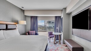 A hotel room with a large bed, a seating area with a table and chairs, a TV mounted on the wall, and a view of the city through the window. - Fiesta Americana México Satélite (Tlalnepantla de Baz)