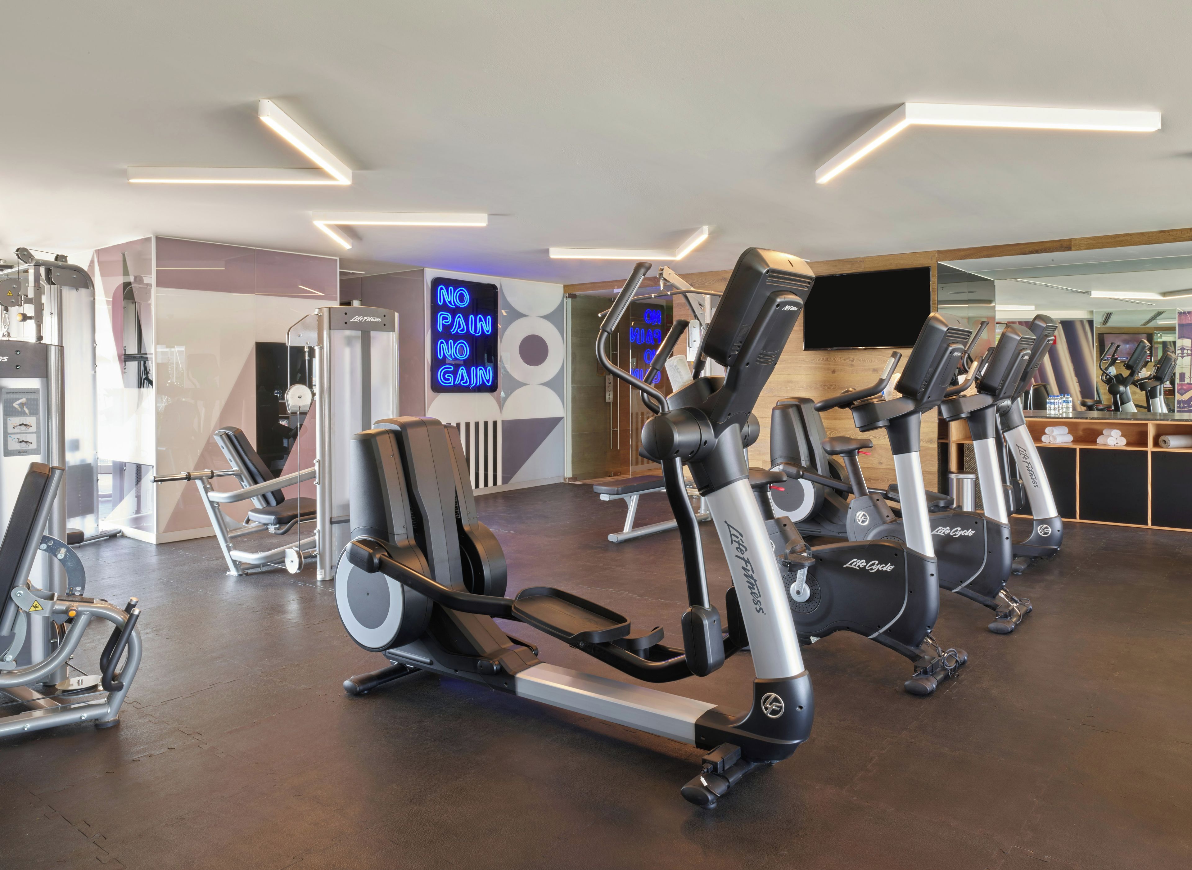 Un gimnasio con máquinas de cardio, un espejo y un letrero de neón.