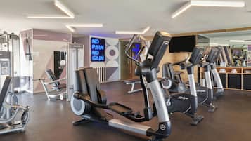 Un gimnasio con máquinas de cardio, un espejo y un letrero de neón.