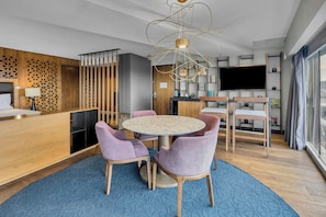 A modern hotel room with a round dining table, purple chairs, a blue carpet, a TV, and a wooden partition with a geometric pattern. - Fiesta Americana México Satélite (Tlalnepantla de Baz)