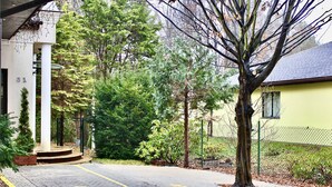 Un camino pavimentado que conduce a un edificio de fachada blanca y un árbol verde en primer plano.