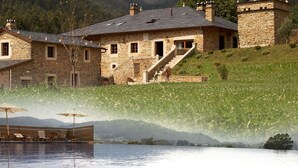 Un edificio de piedra con piscina, rodeado de un exuberante paisaje verde y colinas.