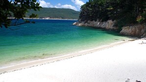 Una playa con agua turquesa cristalina, arena blanca y un acantilado rocoso.
